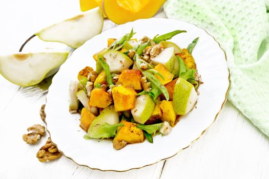 Salad of baked pumpkin, fresh pear, arugula and walnuts, seasoned with honey, balsamic vinegar, spices and vegetable oil in a plate on background of light wooden board