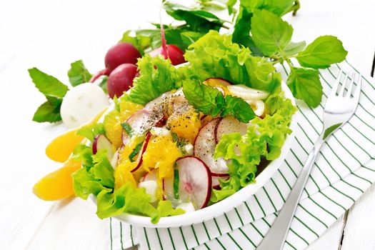 Radish, onion and orange salad with mint, vegetable oil and spices on lettuce in a plate on a napkin on wooden board background