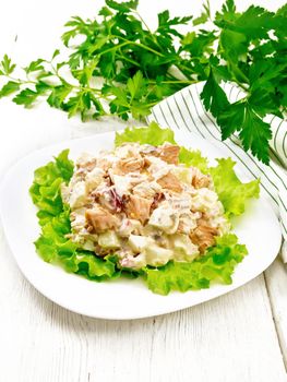 Salad of smoked salmon, cucumber, eggs and sweet pepper seasoned with sour cream on lettuce leaves in a plate, napkin, parsley on light wooden board background