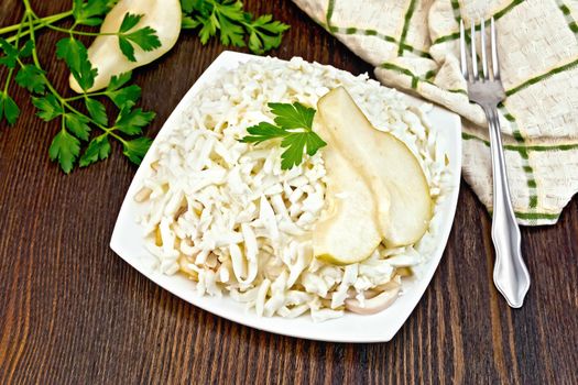 Salad of squid, rice, pears and eggs in a plate, parsley, kitchen towel and fork on the background of wooden boards