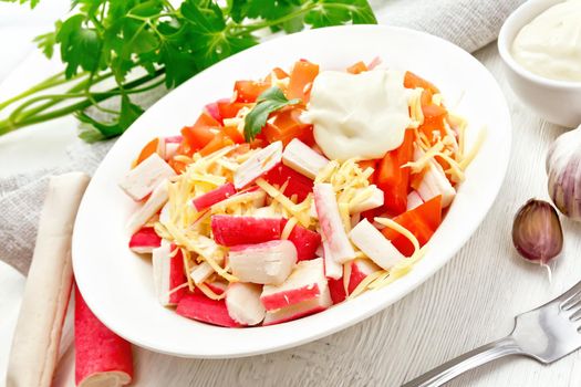 Salad of crab sticks, cheese, garlic and tomatoes with mayonnaise, towel, parsley on the background of a light wooden board