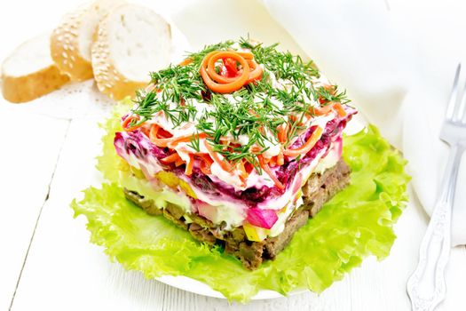 Puff salad with beef, boiled potatoes, pears, spicy Korean carrots, seasoned with mayonnaise and garnished with dill on green lettuce in plate, bread on white wooden board background