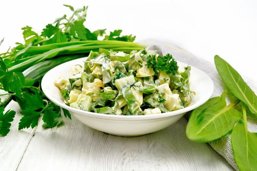 Salad of cucumber, sorrel, boiled potatoes, eggs and herbs, dressed with mayonnaise in a white plate, parsley, green onions and towel against the background of wooden boards