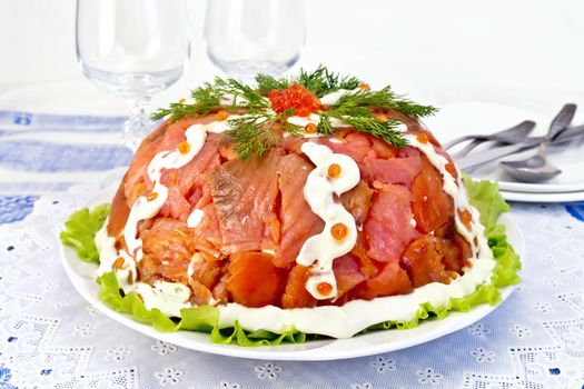 Salad layered with salmon, egg, crab meat and rice, mayonnaise in a plate on a green lettuce on the background of a tablecloth