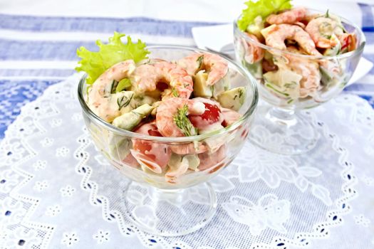 Salad with shrimp, avocado, tomato and mayonnaise, green lettuce in a glass goblet with a silicone white napkin, a plate against the background of blue linen tablecloth