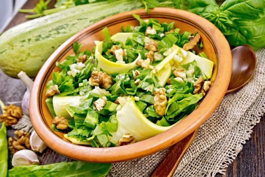 Salad of young zucchini, sorrel, garlic and walnuts, seasoned with vegetable oil in a plate on napkin of sackcloth on a background of dark wooden board