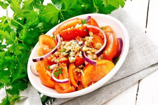 Fresh tomato salad with walnuts and red onions, seasoned with olive oil, vinegar, fenugreek and salt in a plate on a napkin on light wooden board background
