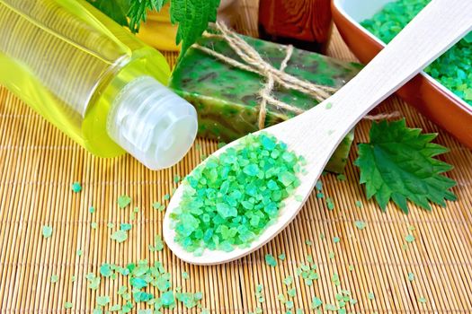 Bath salt in a spoon, homemade soap with twine, oil in the bottle, nettle, shampoo on a background of a bamboo napkin