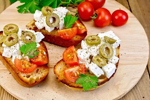 Slices of bread with feta, tomato and olives on a round board, parsley and tomatoes on a wooden table
