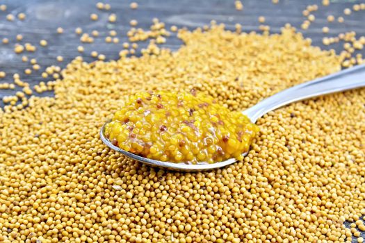 Mustard Dijon sauce in a metal spoon on the seeds against black wooden board