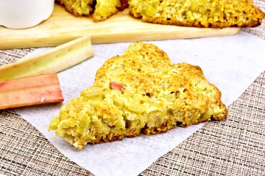 Scones with a rhubarb on parchment and rhubarb scapes against the background of wattled napkin