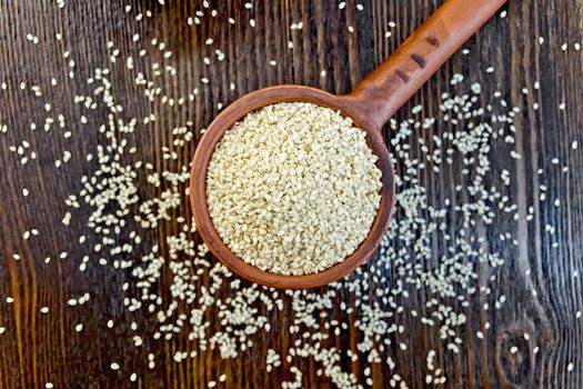 Sesame seeds in a clay ladle on a background of wooden boards on top