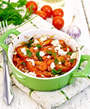 Shrimp and tomatoes baked with salty feta cheese in a green roasting pan on a kitchen towel, garlic on a wooden boards background