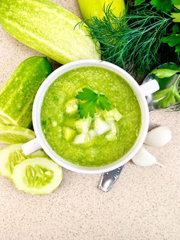 Cucumber soup with green peppers and garlic in a white bowl, parsley on a background of a granite table top