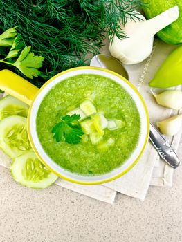 Cucumber soup with green peppers and garlic in a bowl on a yellow napkin, parsley, spoon on a background of a granite table top