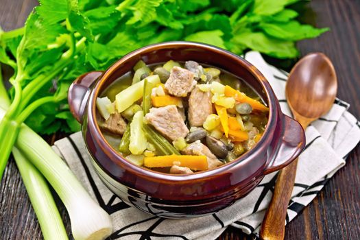 Eintopf soup made from pork, celery, beans, carrots and potatoes with leek in a clay bowl on a napkin on dark wooden board background