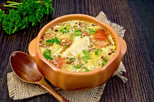 Fish soup with tomatoes, potatoes, pepper and cream in a clay bowl on burlap, parsley on a background of a dark wooden board