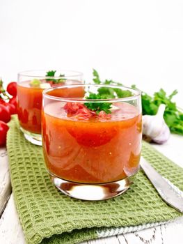 Gazpacho tomato soup in two glasses with parsley and vegetables on the green napkin on the background light wooden boards