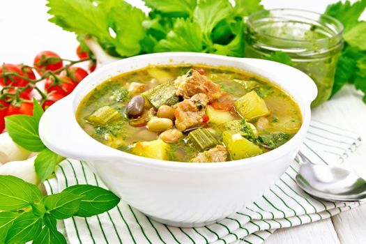 Soup with pisto sauce, lard, tomatoes, zucchini, beans, celery and onions leek in a bowl on a napkin on wooden board background