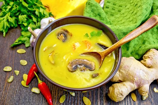 Soup-puree pumpkin with shrimp and mushrooms, spoon in a brown cup, napkin, parsley, hot red pepper pods, pumpkin seeds, ginger root on a dark wooden board