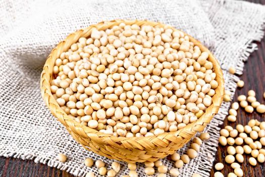 Soybeans in a wicker bowl on a burlap on wooden board background