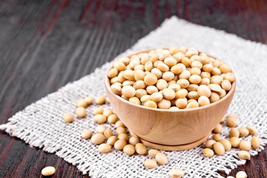 Soy beans in a bowl on sacking on a dark wooden board background