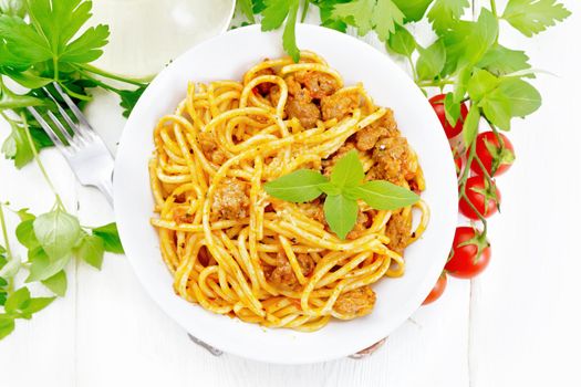 Spaghetti pasta with sauce Bolognese of minced meat, tomato juice, garlic, wine and basil in a plate, vegetable oil, spicy herb on a wooden board background from above