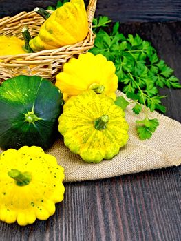 Yellow and green squash on sackcloth and wicker basket, a bunch of parsley on a dark wooden board