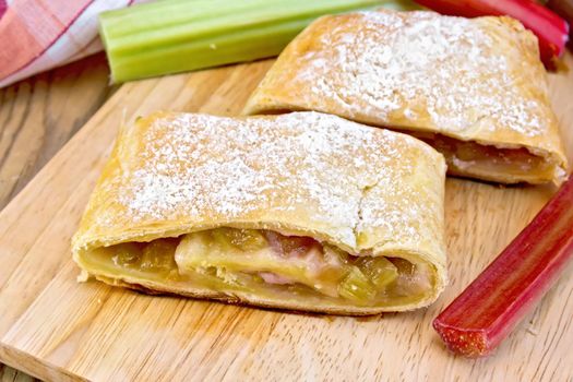 Strudel with rhubarb, napkin and stems on a wooden boards background
