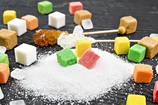 Sugar of white, brown, pink, green, yellow and different shapes on a wooden board background
