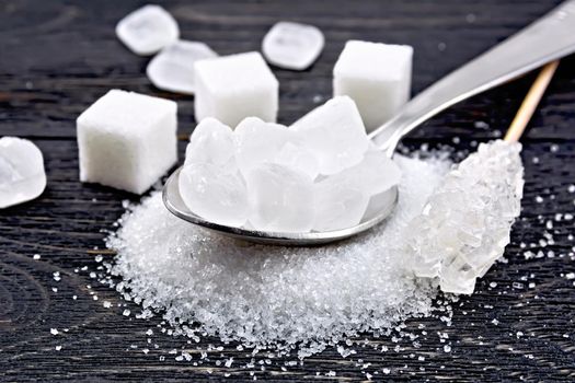 Sugar white crystals in a metal spoon, granulated and cubes on a black wooden board background