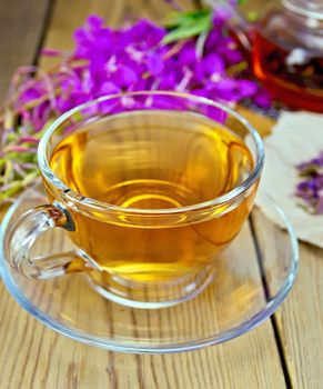 Herbal tea in a glass cup and teapot, fresh flowers fireweed, fireweed flowers dry on paper on a wooden boards background