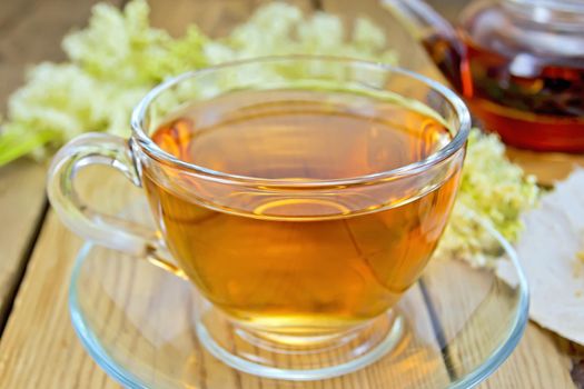 Meadowsweet tea from a glass cup and teapot, dried flowers on paper meadowsweet, meadowsweet fresh flowers on the background of wooden boards