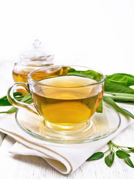 Herbal tea with sage in a glass cup and teapot on a napkin on wooden board background