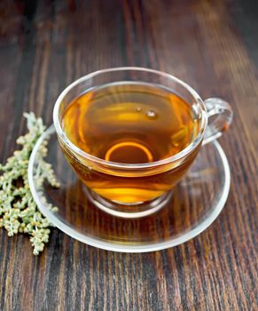 Herbal tea from wormwood in a glass cup with a saucer on a wooden boards background