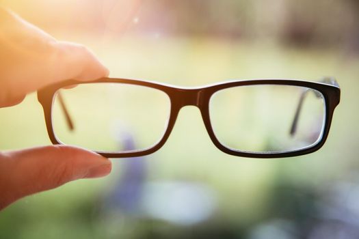 Young man holding his glasses outdoors, blurry background