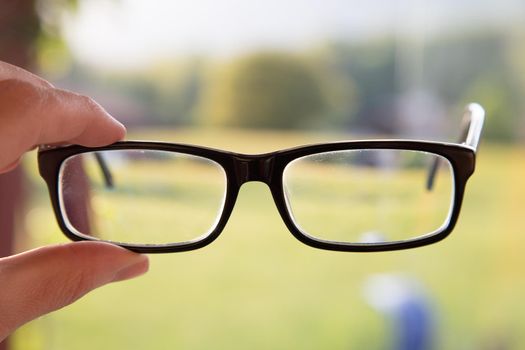 Young man holding his glasses outdoors, blurry background