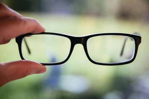 Young man holding his glasses outdoors, blurry background