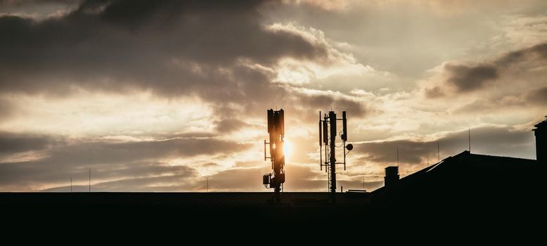 Silhouette of communication or cell tower on the rooftop of a building, evening sunshine