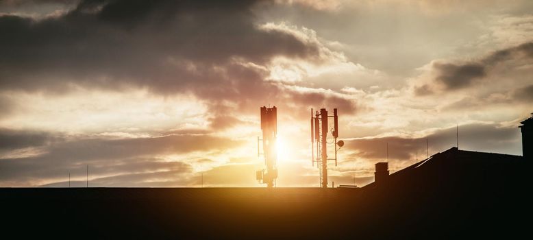 Silhouette of communication or cell tower on the rooftop of a building, evening sunshine