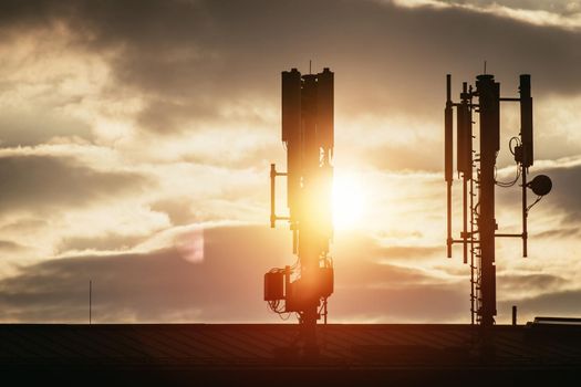 Silhouette of communication or cell tower on the rooftop of a building, evening sunshine