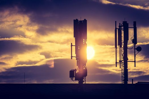 Silhouette of communication or cell tower on the rooftop of a building, evening sunshine