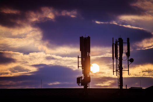 Silhouette of communication or cell tower on the rooftop of a building, evening sunshine