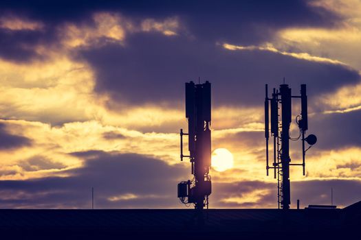 Silhouette of communication or cell tower on the rooftop of a building, evening sunshine