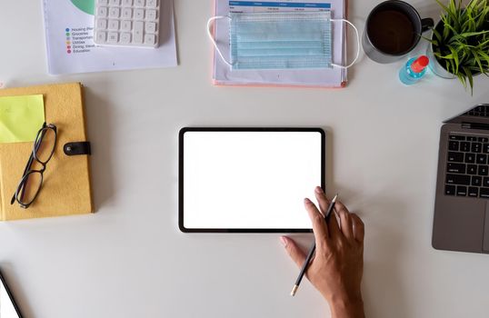 White office desk table with surgical face mask and sanitizer bottle or alcohol gel with calculator isolated on white background, Hand of man using tablet with blank screen at home.