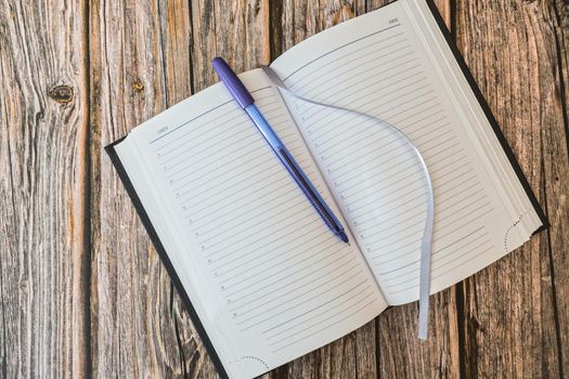 Opened diary or notebook for notes with pen on wooden table top view