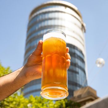 Man holding beer mug, glass with building background