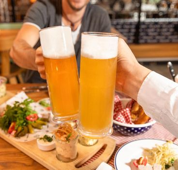 Clinking beer mugs close up, snacks on the table