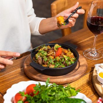 Woman eating tasty meat meal on the wooden plate with red wine