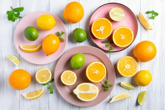 Close-up of whole and cut citrus fruits on pink ceramic plates on a painted natural wood surface. Selective focus.